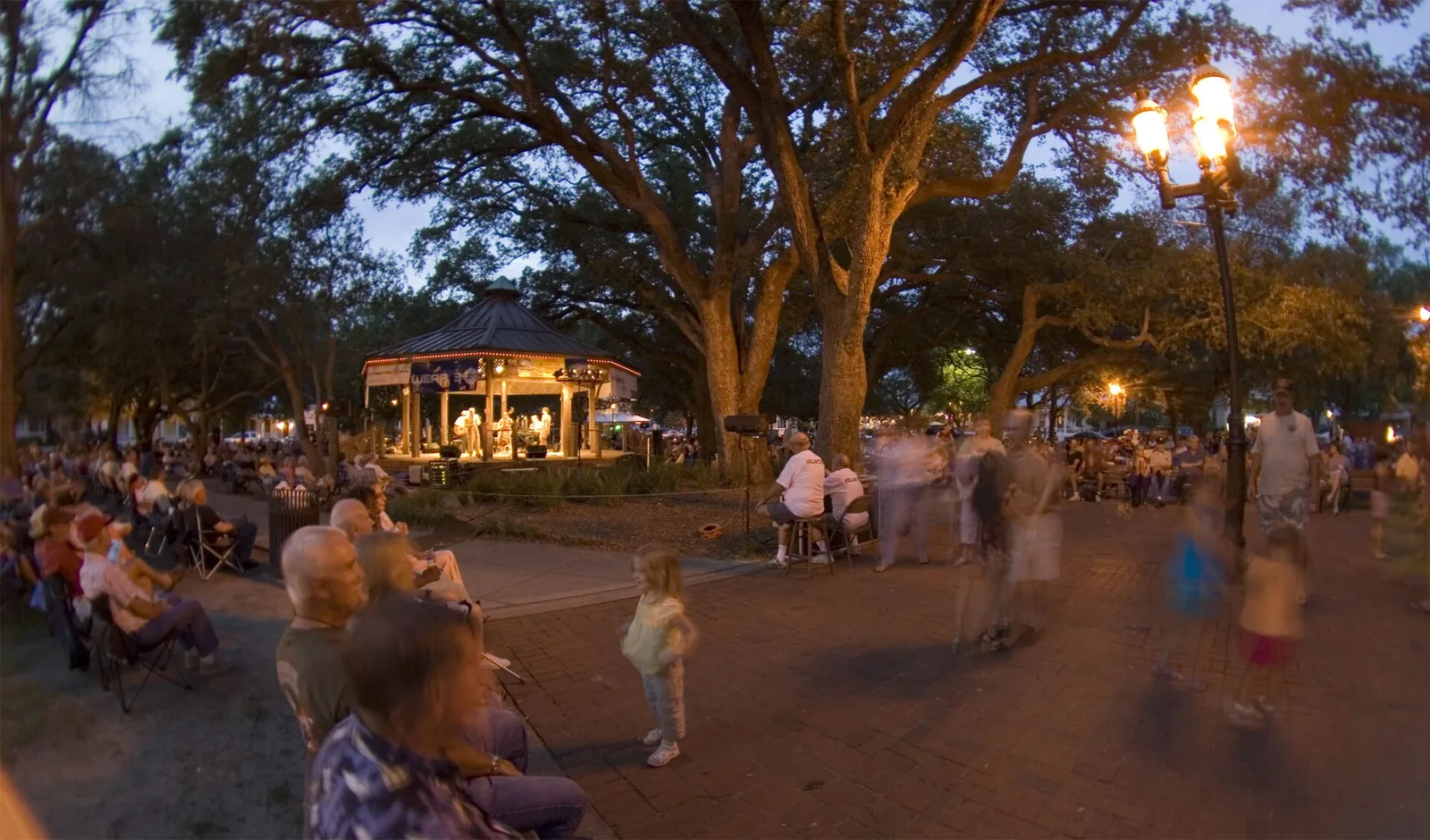 Crowds gather under the oaks at dusk for a band concert in Seville Square, home of the Great Gulfcoast Arts Festival.